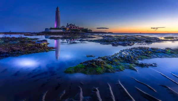 Futuristic lighthouse surrounded by vibrant blue water at sunset.